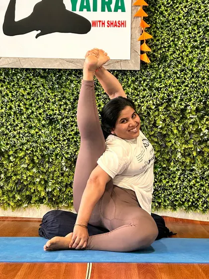 A student smiles while practicing a seated hip-opening pose on a bolster, demonstrating joy and comfort in her practice.