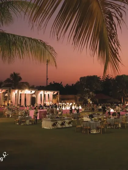 An overview of an outdoor reception at dusk. The warm lighting, elegant seating, and lush green lawn create a magical and romantic atmosphere for an evening of celebration.