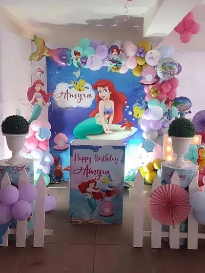 An under-the-sea 'Little Mermaid' birthday party with a custom backdrop, character cutouts, and themed props like a white picket fence.