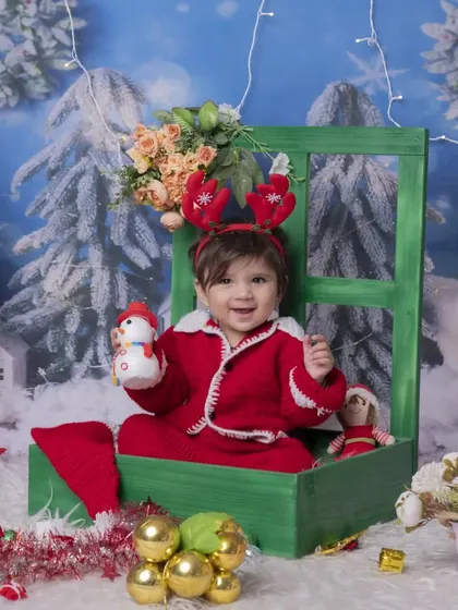 A cute baby in a Santa suit and reindeer antlers, sitting in a green box surrounded by Christmas decorations. This playful setup results in adorable holiday photos.