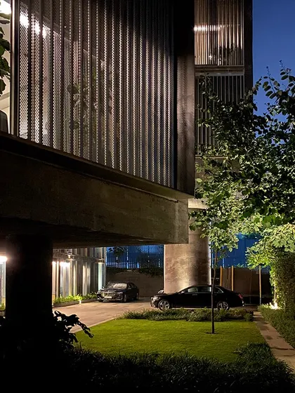 The driveway and entrance of the Jenga House at night. Strategic lighting emphasizes the texture of the concrete and the building's geometric forms, creating a dramatic nocturnal presence.