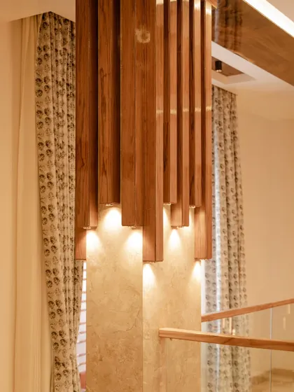 A close-up of the wooden pillar light installation, showing how the warm light accentuates the texture of the stone wall behind it.