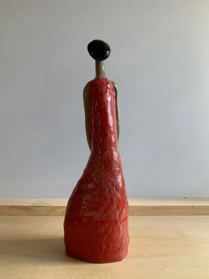 A back view of the "Damn Red Woman" sculpture. Even from behind, the posture and form convey a story of carrying burdens with grace.
