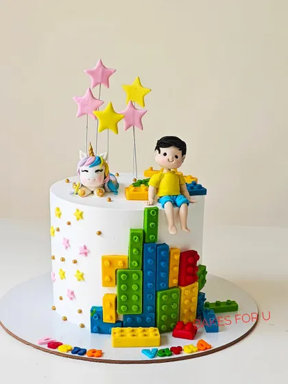 A special cake designed for twins, featuring a boy and a unicorn sitting atop a tower of colorful Lego blocks. This design cleverly combines two different themes into one cohesive and celebratory cake.