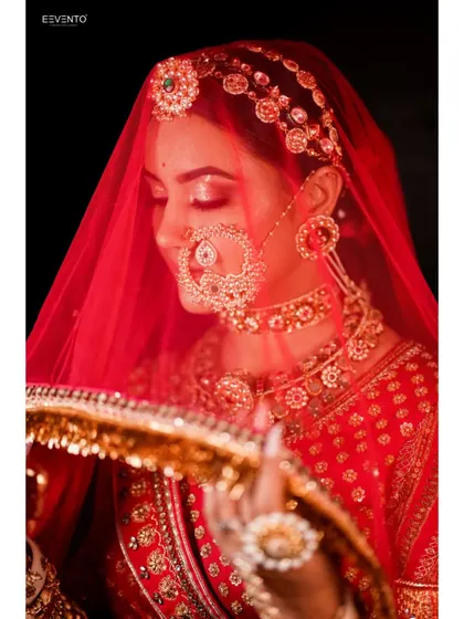 A candid moment under the veil. The soft lighting highlights the shimmer on the eyelids and the delicate details of the nath, creating a dreamy and romantic bridal portrait.