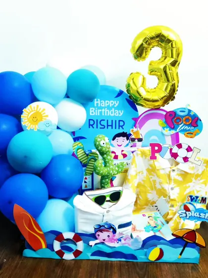 Make a splash with this fun pool party themed hamper for a 3rd birthday. The entire setup is blue, featuring a toy, a shirt, and decorations like a surfboard and lifebuoy to set the scene.