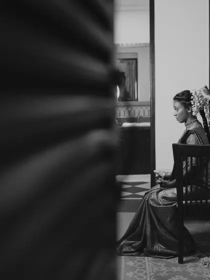 A pensive, black and white portrait of a bride sitting alone, captured from a distance, creating a quiet and cinematic moment of reflection.