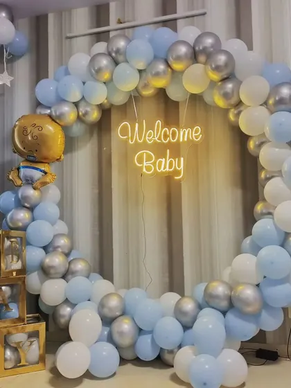 A "Welcome Baby" setup with a blue, white, and silver balloon ring, neon sign, and 'BABY' blocks.