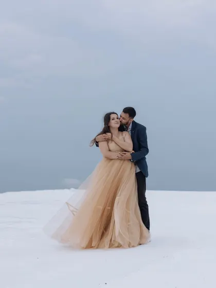 A breathtaking portrait in a surreal, snow-like landscape. The bride's flowing golden gown provides a stunning contrast against the white ground, creating a truly magical and ethereal image.