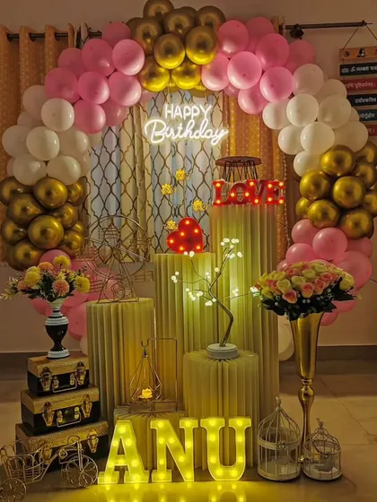 An elegant and romantic birthday decoration perfect for a surprise at home. The pink, white, and gold balloon arch, combined with light-up letters and props, creates a warm and celebratory feel.