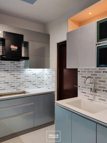 A kitchen with glossy light blue cabinets and a unique mosaic tile backsplash in shades of grey and white. The open niche above the cabinets is finished in a bright orange for a playful pop of color.