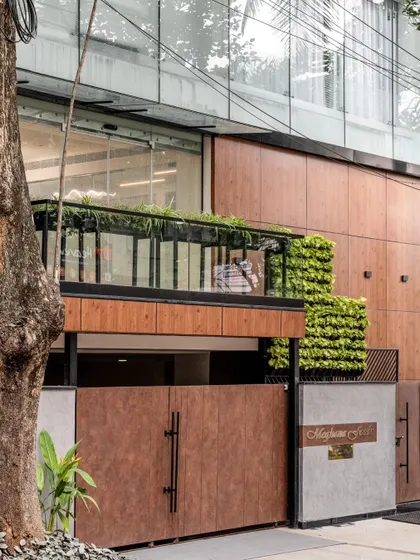 The exterior of the Meghana Foods office in Koramangala, featuring a metal staircase lined with a vertical garden. The facade commands attention with its blend of wood-paneled cladding, glass, and lush greenery, creating a statement of modern corporate design.
