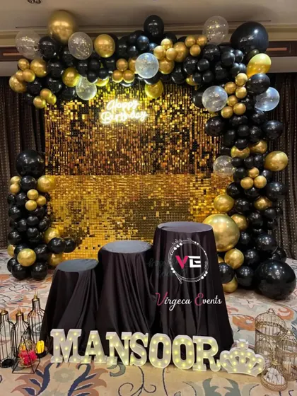 A glamorous birthday setup with a gold shimmer wall and a black and gold balloon arch, perfect for a milestone celebration.