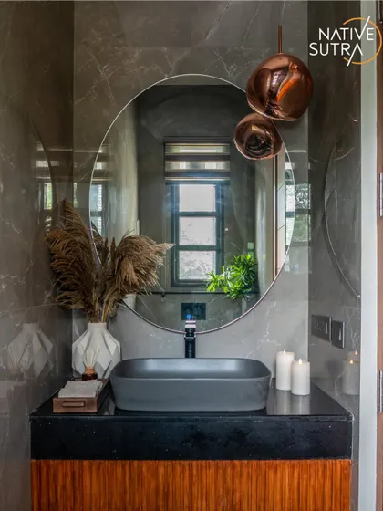 A powder room that makes a statement. The design features a fluted wooden vanity, a matte black vessel sink, and dramatic copper pendant lights against moody grey marble walls for a look of sophisticated luxury.