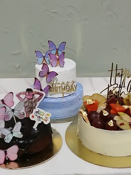 A display of three different birthday cakes: two with butterflies and one with fresh fruit.