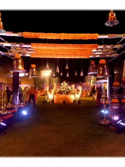 The entrance to the Banaras Ghat-themed event, featuring walls with niches holding small idols, hanging temple bells, and marigold garlands.