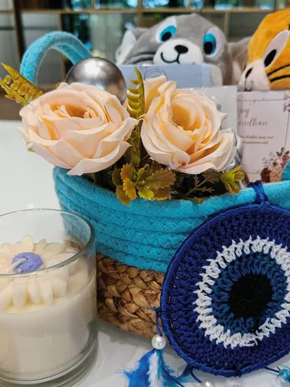 A closer look at the Tom & Jerry Rakhi hamper, showing the evil-eye dreamcatcher and a beautiful floral-scented candle, perfect for a sister who loves aesthetic decor.