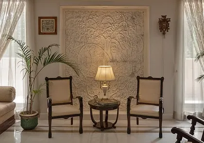 This seating nook in the Kaira residence is a study in texture and light. A large, textured art piece serves as a focal point, flanked by classic chairs and bathed in soft, natural light from sheer curtains, creating a perfect corner for quiet reflection.