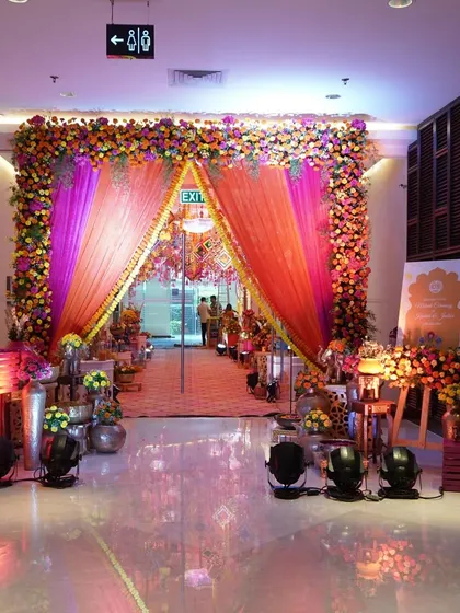 A vibrant and festive entrance for a Haldi or Mehendi ceremony. The archway is bursting with colorful flowers and rich orange drapes, creating a joyful and energetic welcome for guests.