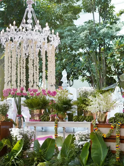 A beautiful view of the decor, showing the lush greenery of banana plants framing a stunning floral chandelier. This blend of rustic and royal elements was a key feature of the design.
