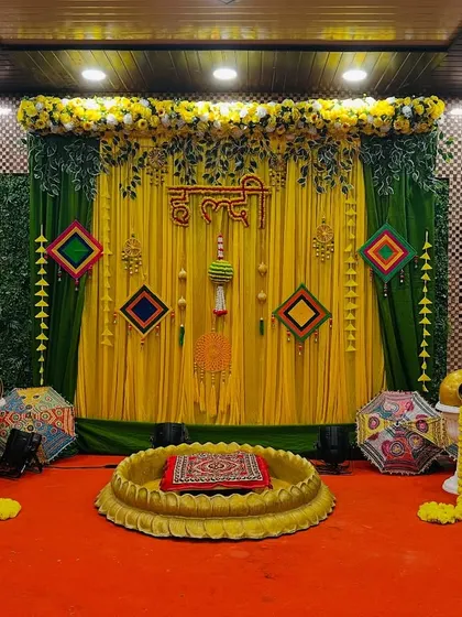 A complete view of a haldi stage setup in a banquet hall. The decor features a green and yellow theme with traditional hangings and a lotus seating area.