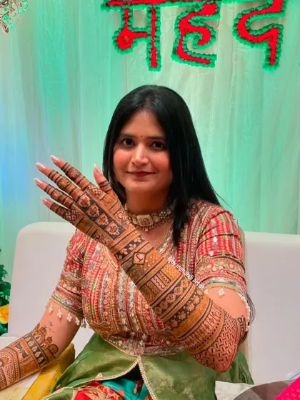 A happy bride showing off her full-arm mehndi, which features a mix of traditional patterns and personalized initials.
