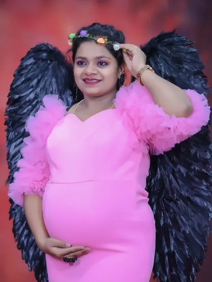 A beautiful maternity photo featuring a woman in a pink gown and black angel wings, creating a striking and memorable image.