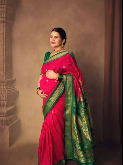 A full-length portrait showcasing the beautiful drape of the Paithani saree against a classic, painted backdrop.
