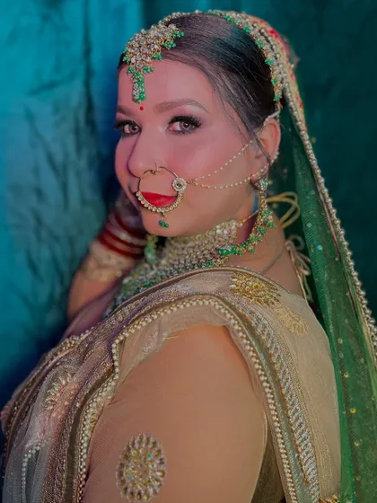 A stunning bridal look with a green and gold saree. The makeup is bold and defined, with a traditional nath and maang tikka completing the look.