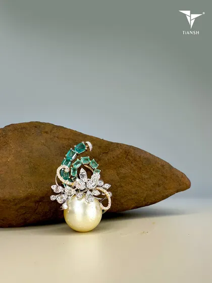 A closer view of the pearl, emerald, and diamond brooch. The swirl of emeralds and diamonds around the central pearl creates a dynamic and organic feel, like a wave cresting.
