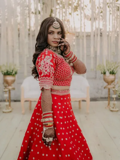 A confident and beautiful pose. The open hairstyle with soft waves adds a modern touch to the traditional red lehenga look.