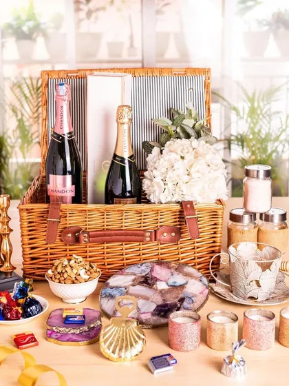 An extravagant wedding gift arrangement featuring two bottles of champagne, gold candelabras, agate coasters, and numerous other luxury items in a large picnic basket.