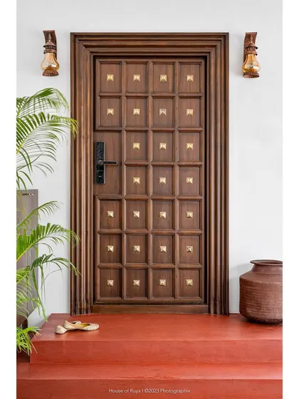 The entrance to 'Mina Nivas' sets a tone of retrospective elegance. The red oxide steps, a nod to traditional South Indian homes, lead to a colossal teak door studded with brass embellishments. It’s a portal that hints at the blend of old and new within.