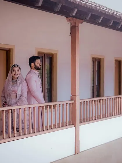 The couple in their matching pink wedding attire, posing on a rustic balcony, creating a serene and stylish portrait.