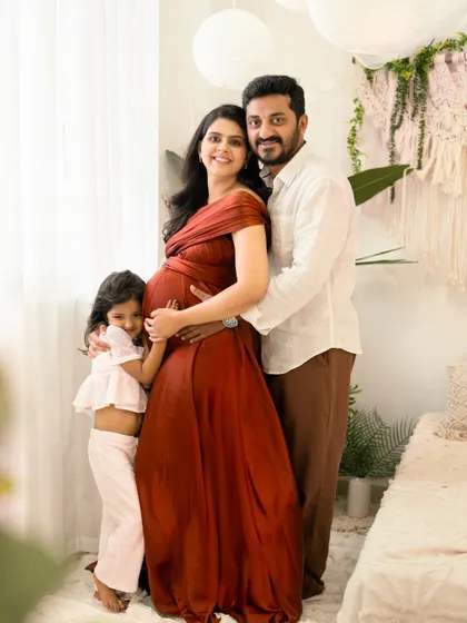 A full family portrait in a bright and airy room. The daughter hugs her mother's baby bump while the father embraces them both, creating a picture of a happy, growing family.