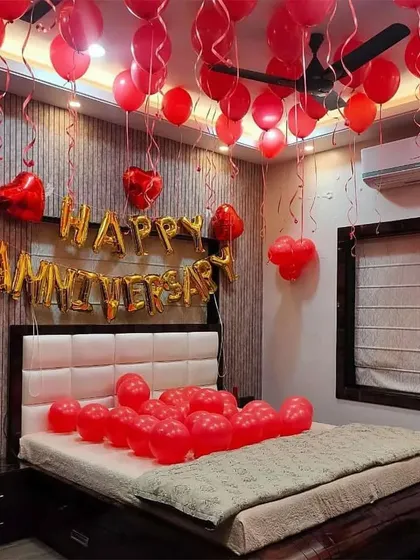 A full-on romantic anniversary surprise with a room filled with red balloons. The setup includes 'Happy Anniversary' foil letters above the bed and helium balloons floating to the ceiling, creating an immersive and celebratory feel.