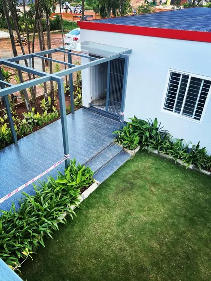 This image shows a simple yet effective landscape and architecture integration. A small patio with a pergola frame is surrounded by a neat lawn and border planting, creating a clean and functional outdoor space.