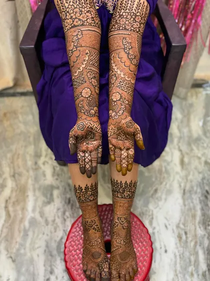 A full view of a bridal mehendi session, showing the intricate work on both the hands and feet. The leg design features a simple forest-like border which is very unique.