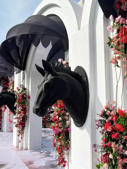 A wall of black horse-head sculptures emerging from white arches, adorned with beautiful pink and red flowers. This dramatic installation served as a stunning photo backdrop.