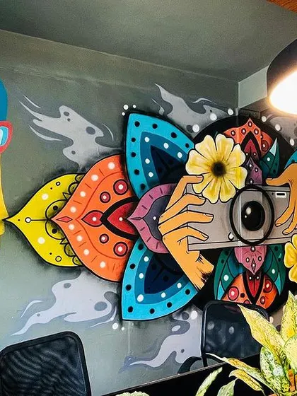 This view shows how the mural interacts with the studio's interior, with the central camera artwork framed by the abstract portraits. The plants in the foreground add a nice natural element.