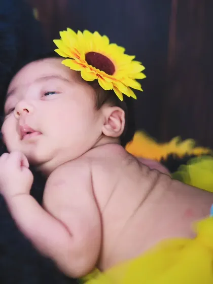 A newborn rests peacefully, adorned with a sunflower headband. We use simple floral props to add a bright and cheerful touch to our sessions.