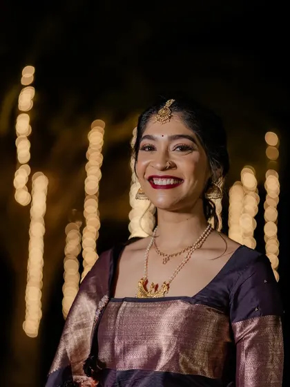 A beautiful nighttime portrait of a Coorgi bride. The bokeh from the lights creates a magical effect, highlighting her happy smile and bold red lip.