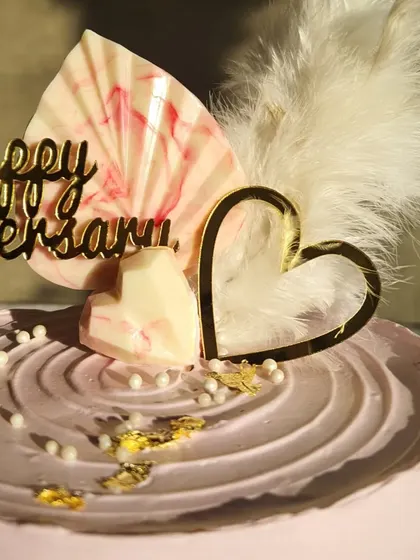 A detailed shot of the toppers on the pink ombre anniversary cake, including the feather and chocolate heart.