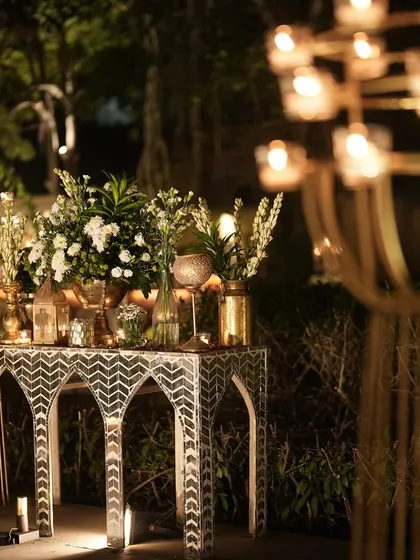 An elegant console table with an intricate inlay pattern, adorned with brass vases, white florals, and candles for the Retro Sufi sangeet.