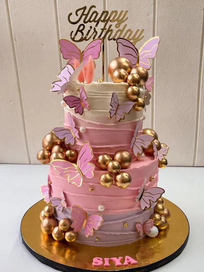 Fluttering into celebration with this dreamy two-tiered butterfly birthday cake. The design features shades of pink buttercream, delicate butterflies, and golden spheres for a touch of glam.