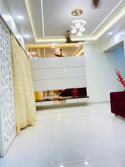 A wider view of the living room, showing the false ceiling with dual-tone lighting and a modern chandelier, creating a layered and luxurious lighting scheme.