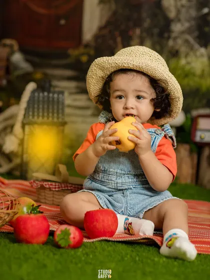 A little one in a straw hat enjoys an apple during the magical picnic session.