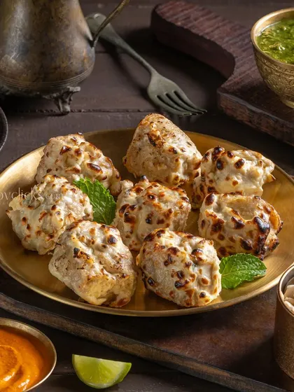 Creamy and tender Chicken Malai Tikka, served on a brass plate with various dips.