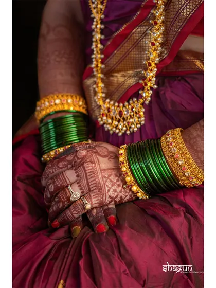 A close-up on the bride's hands, showcasing her beautiful green bangles, gold jewelry, and intricate mehndi design.