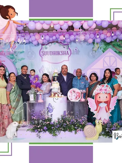 A happy family portrait at a magical fairy-themed birthday party. The family is gathered in front of the custom-designed stage, complete with a fairy house, whimsical characters, and enchanting purple floral arrangements.
